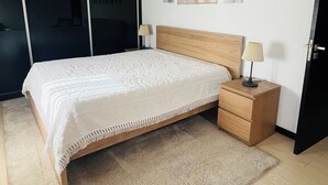 A bedroom with a large bed, a nightstand, a lamp, a wooden headboard, a wall with framed pictures, and a sliding door. - NocasHouse Porto (Campo)