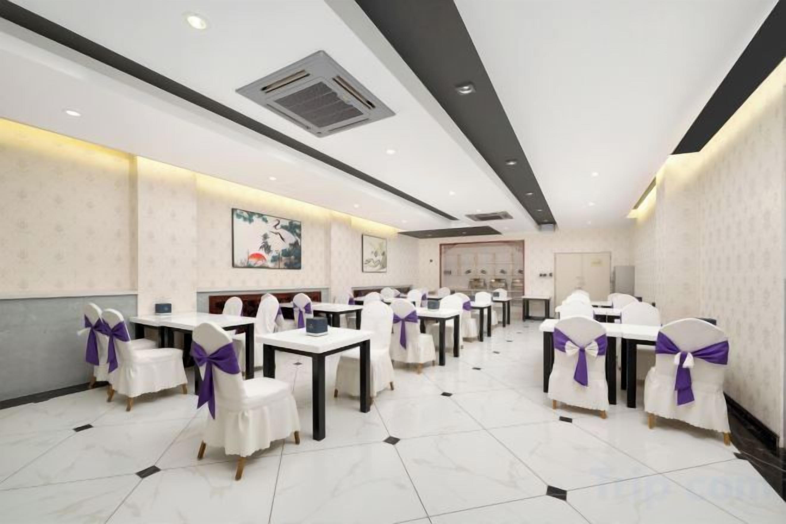 A hotel dining area with tables and chairs, a ceiling vent, and a door in the background.