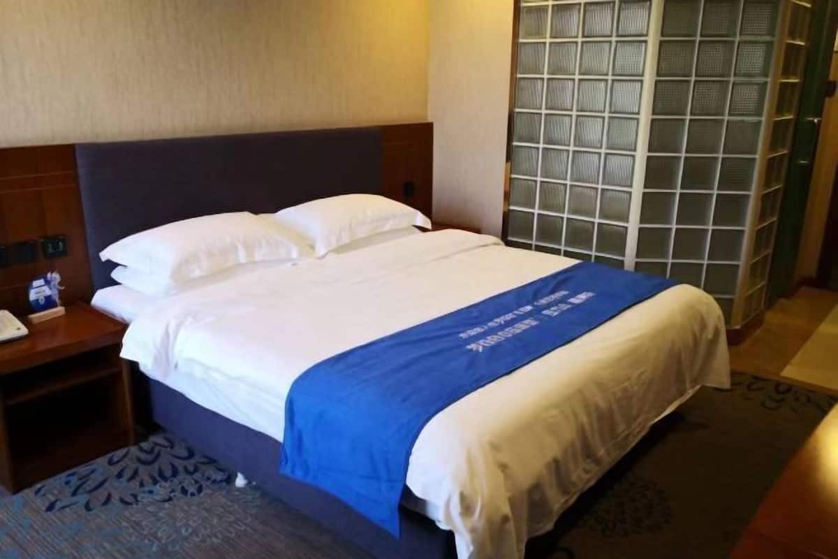 Habitación de hotel con cama, mesita de noche, toalla azul y ventana con vista a un edificio.