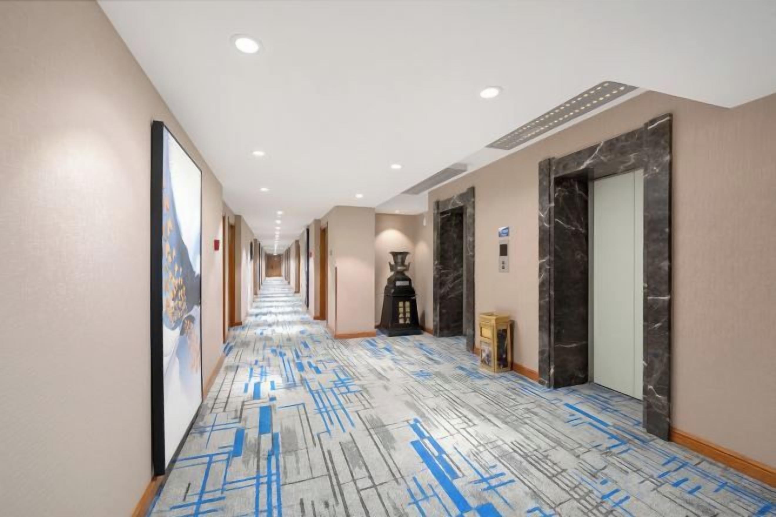 Un pasillo de hotel con alfombra estampada, un espejo grande y una puerta con marco de mármol.