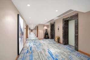 A hotel hallway with a patterned carpet, a large mirror, and a door with a marble frame. - Diyu Mansion Hotel (Harbin Central Street) (Harbin)