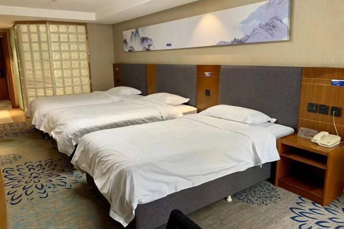 Habitación de hotel con dos camas, una obra de arte grande en la pared y una alfombra con motivos florales.