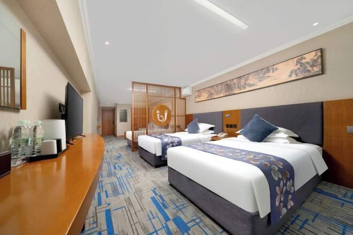 Habitación de hotel con dos camas, un escritorio, un televisor y un biombo decorativo.