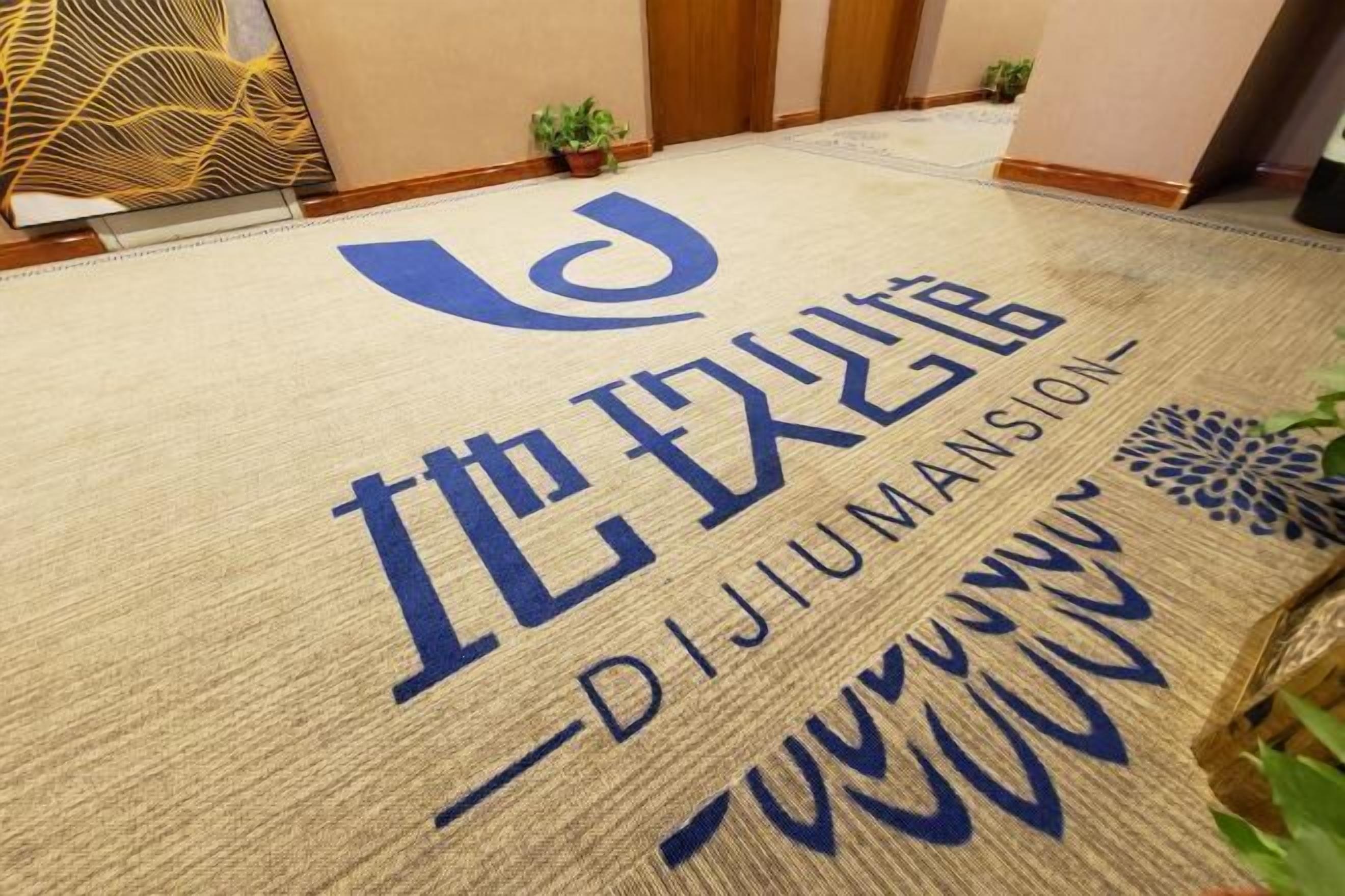A hotel entrance with a doormat displaying the name "DIJUMANSION" in large blue letters.