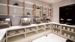 A buffet setup with multiple serving stations, shelves with plates and bowls, and a dark wooden door. - Diyu Mansion Hotel (Harbin Central Street) (Harbin)