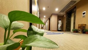 A hotel corridor with carpeted flooring, potted plants, and a marble statue. - Diyu Mansion Hotel (Harbin Central Street) (Harbin)