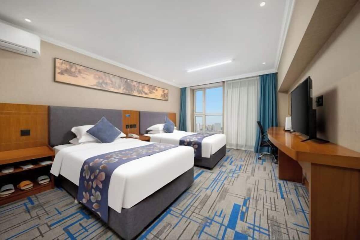 Habitación de hotel con dos camas, un escritorio, un televisor y vistas a la ciudad.
