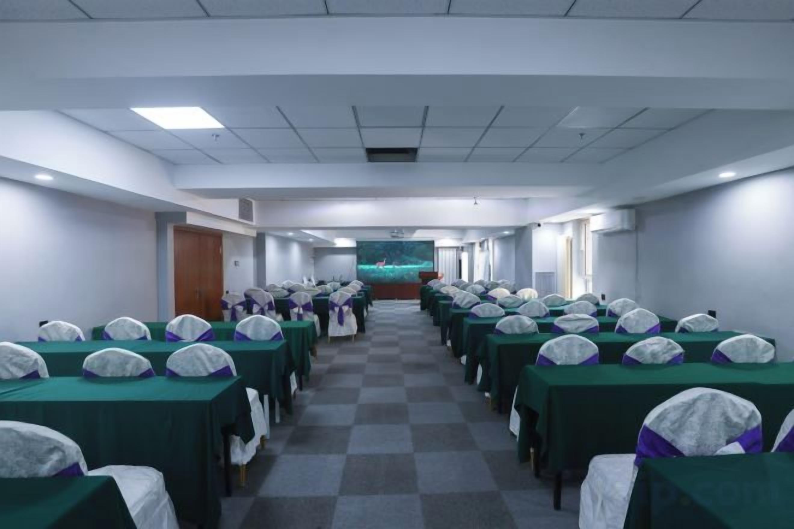 A conference room with rows of tables and chairs, a stage at the front, and a projector screen.
