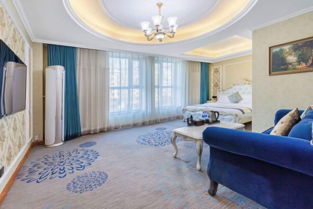 Una habitación de hotel con una cama grande, un sofá azul, una mesa de centro y un candelabro.