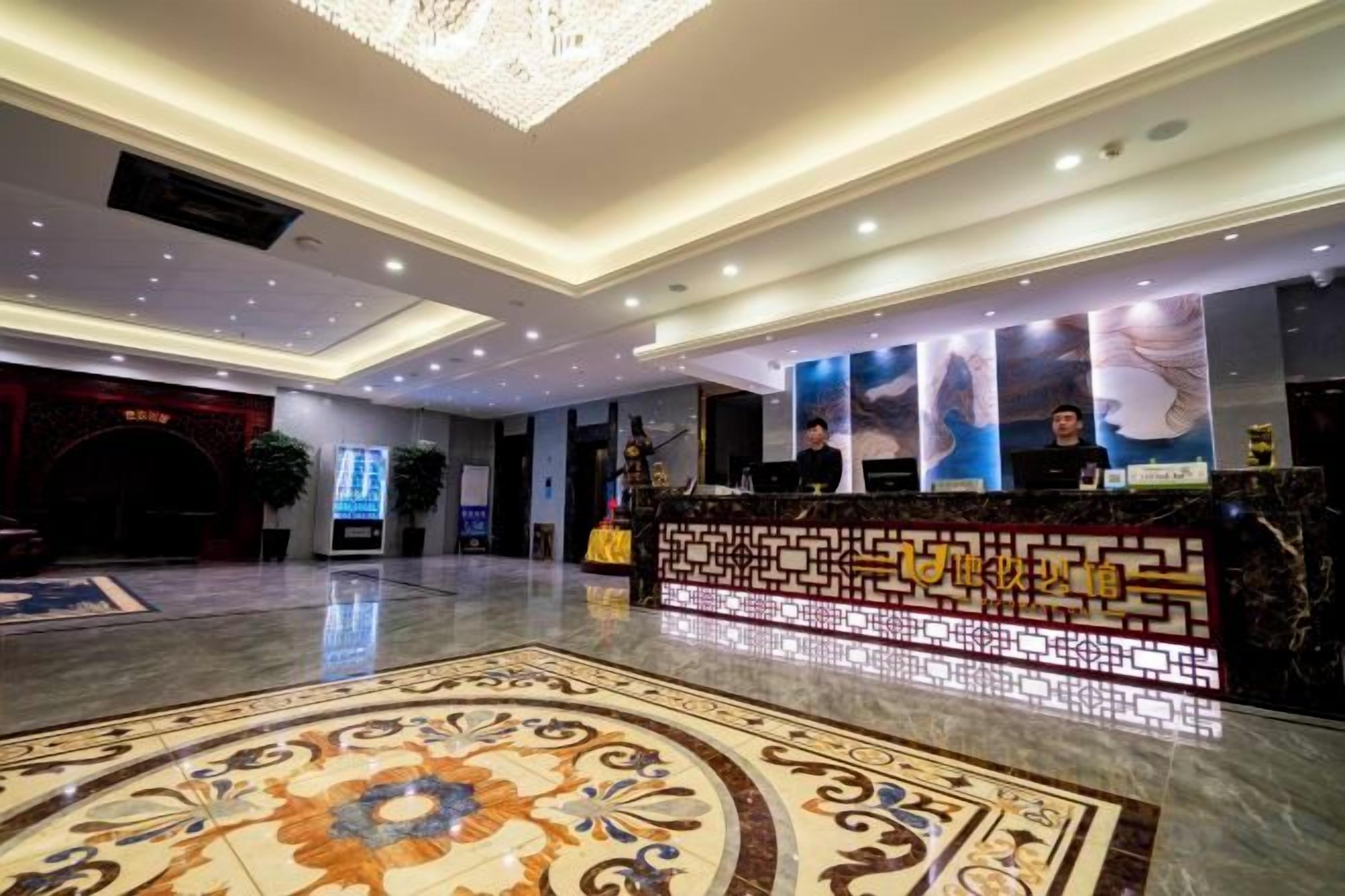 Un hall d’hôtel comprenant un comptoir d’accueil, une grande moquette décorative et un lustre moderne.