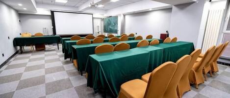 Una sala de conferencias con mesas y sillas, una pantalla de proyector y una pantalla para presentaciones.