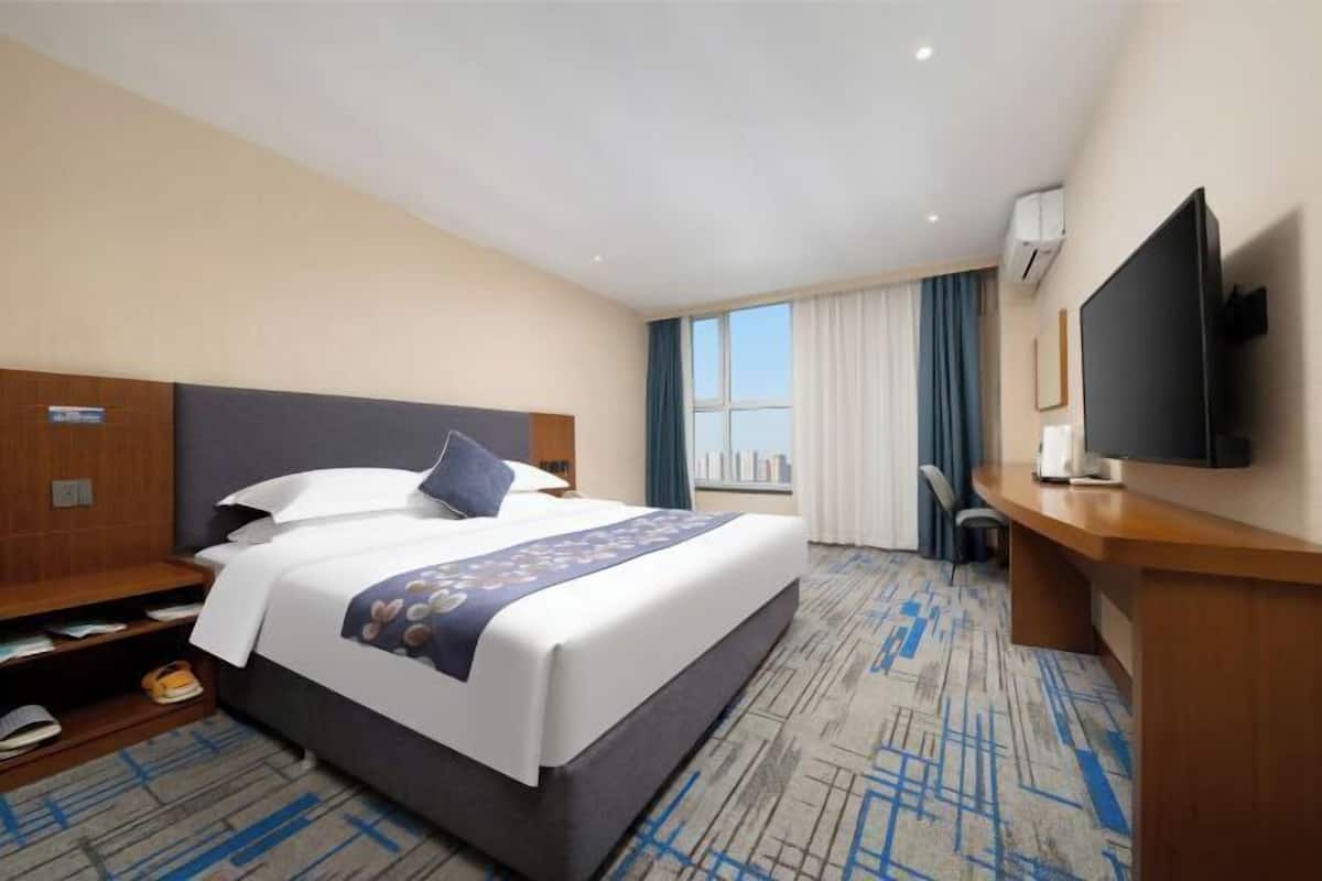 Una habitación de hotel con cama, escritorio, televisión y ventana con cortinas.