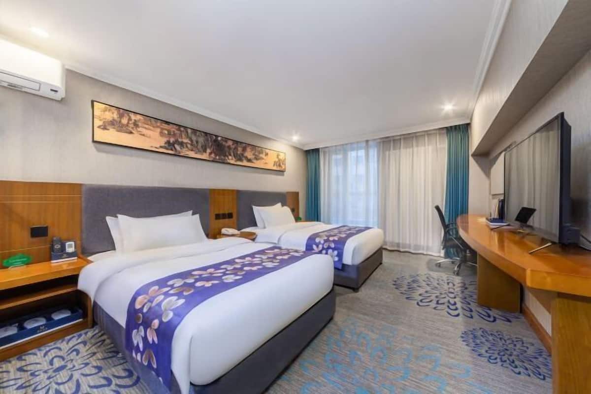 Una habitación de hotel con dos camas, un escritorio, un televisor y un cuadro en la pared.
