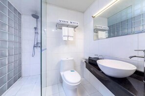 A modern bathroom with a glass shower enclosure, a white toilet, and a large white sink with a black countertop. - Diyu Mansion Hotel (Harbin Central Street) (Harbin)