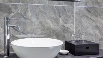 Un baño moderno con un lavabo de cerámica blanca, un grifo de cromo y un calentador eléctrico negro sobre una encimera de mármol.