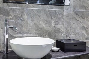 Un baño moderno con un lavabo de cerámica blanca, un grifo de cromo y un calentador eléctrico negro sobre una encimera de mármol.