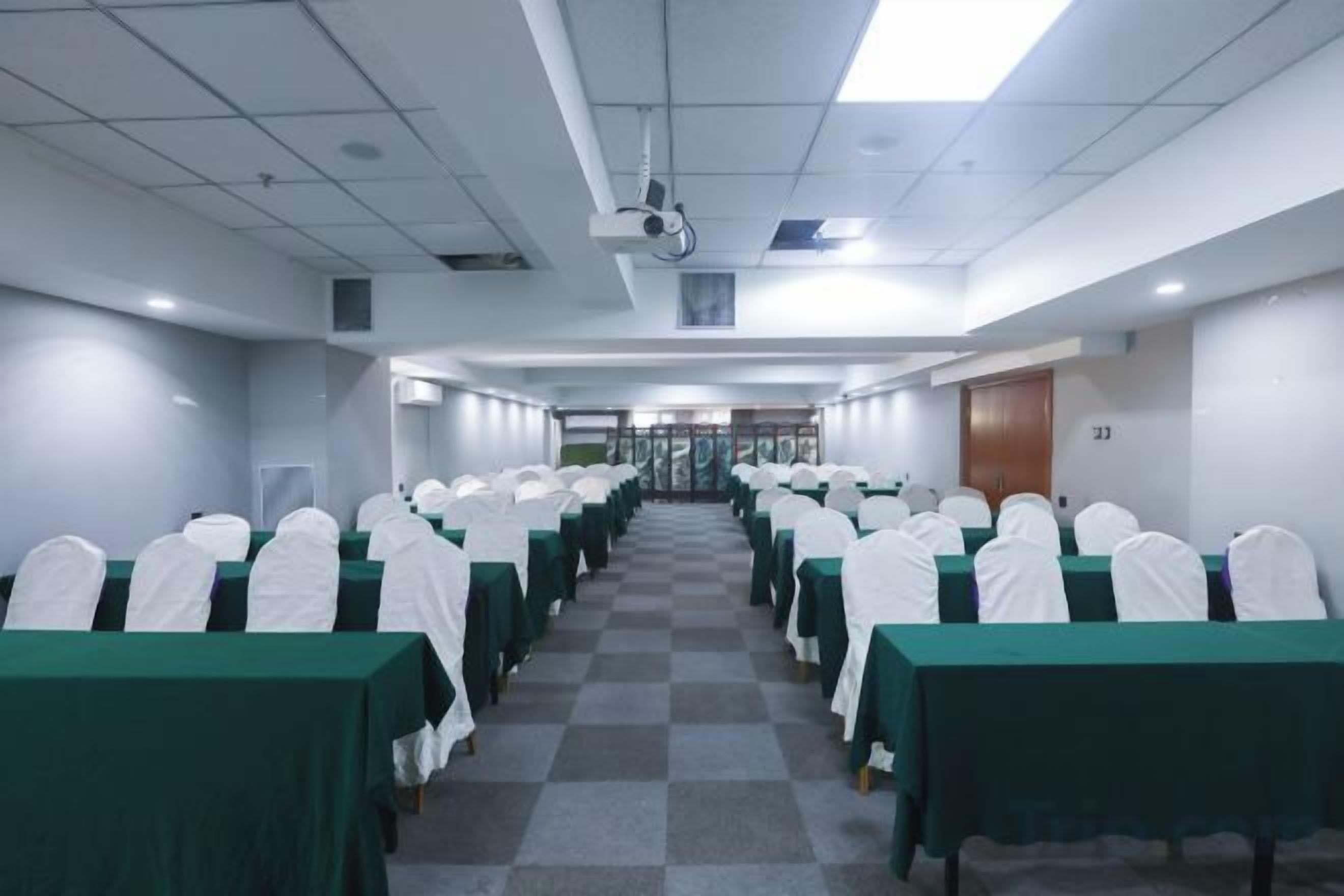 Uma sala de conferências com fileiras de mesas e cadeiras, um projetor no teto e uma porta com a inscrição '23' à direita.