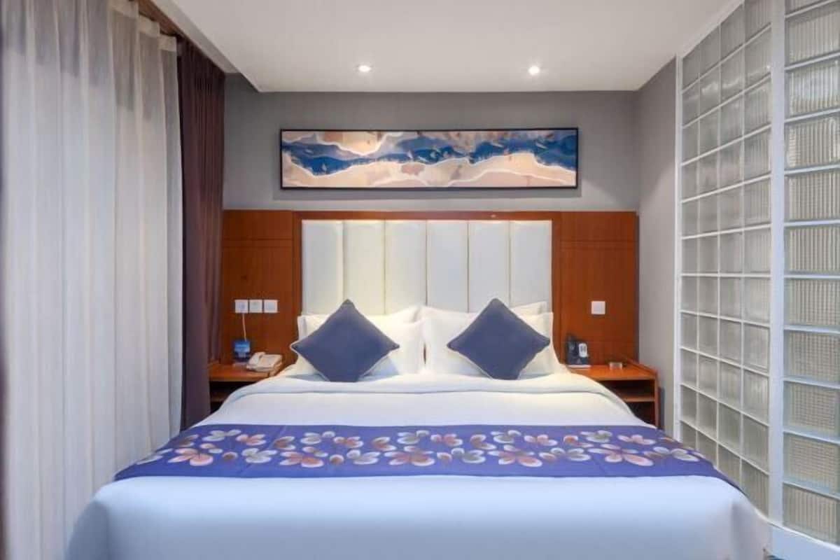 Una habitación de hotel con una cama grande, cabecera con listones verticales, una obra de arte colgada en la pared y un ventanal con persianas.