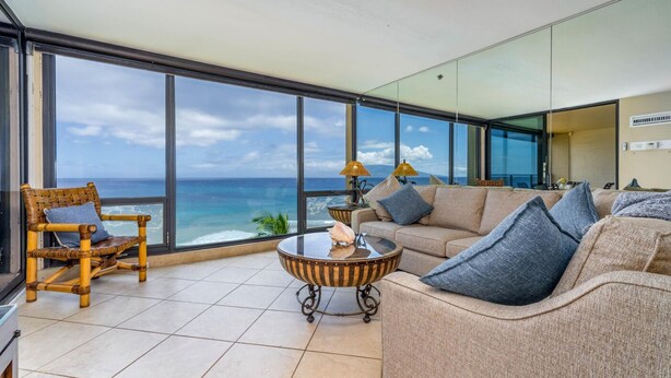 Un salon moderne doté d’une grande baie vitrée donnant sur l’océan, et aménagé avec un canapé, des fauteuils et une table basse.