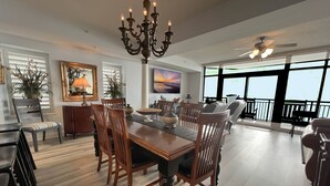 Un comedor con mesa de madera, sillas, una araña y vistas al exterior a través de amplios ventanales.