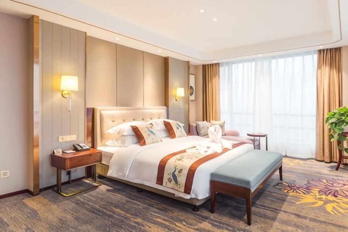 A hotel room with a large bed, bedside tables, a desk, and a window with curtains.