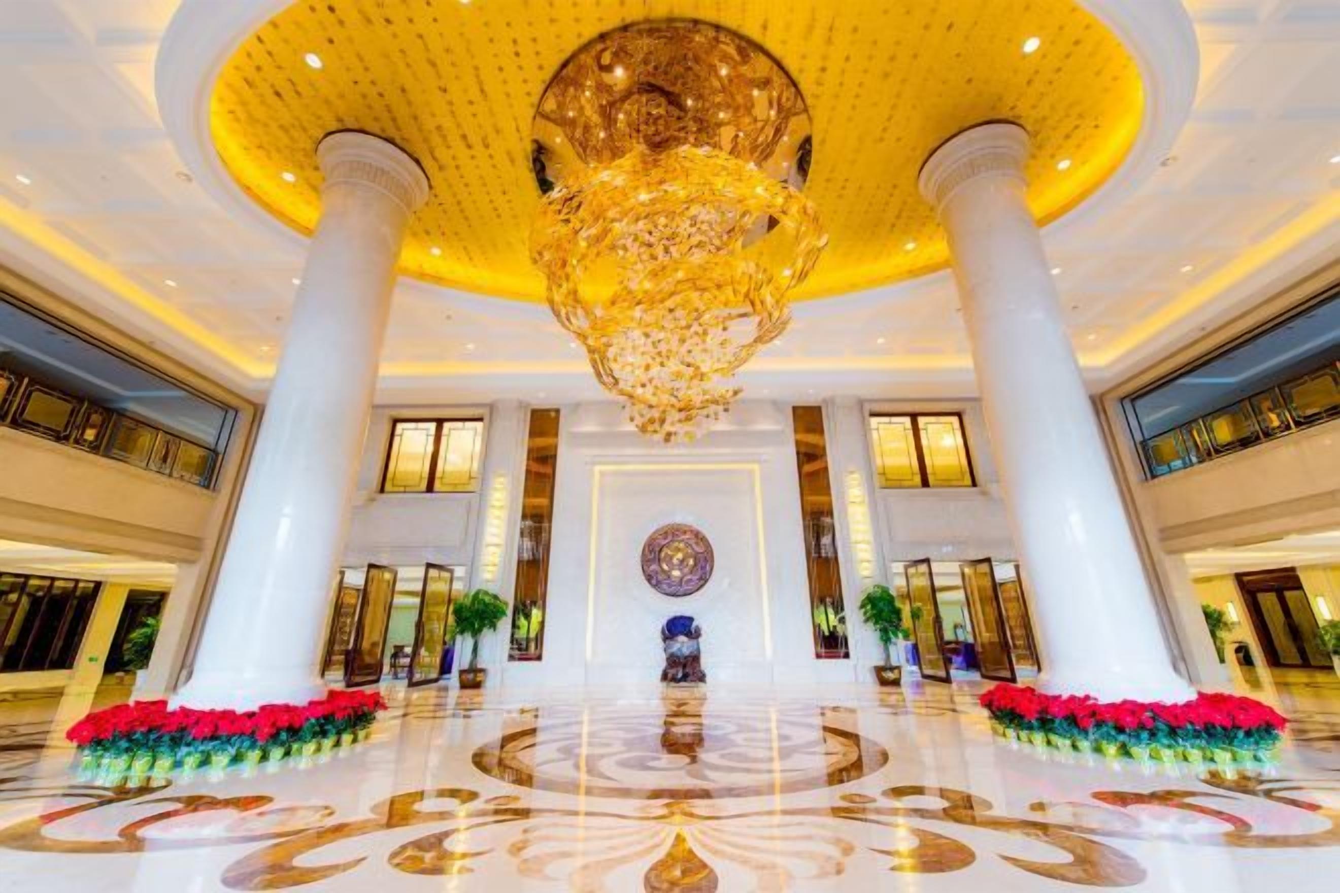 A grand lobby with a large chandelier, white columns, and a central floral arrangement.