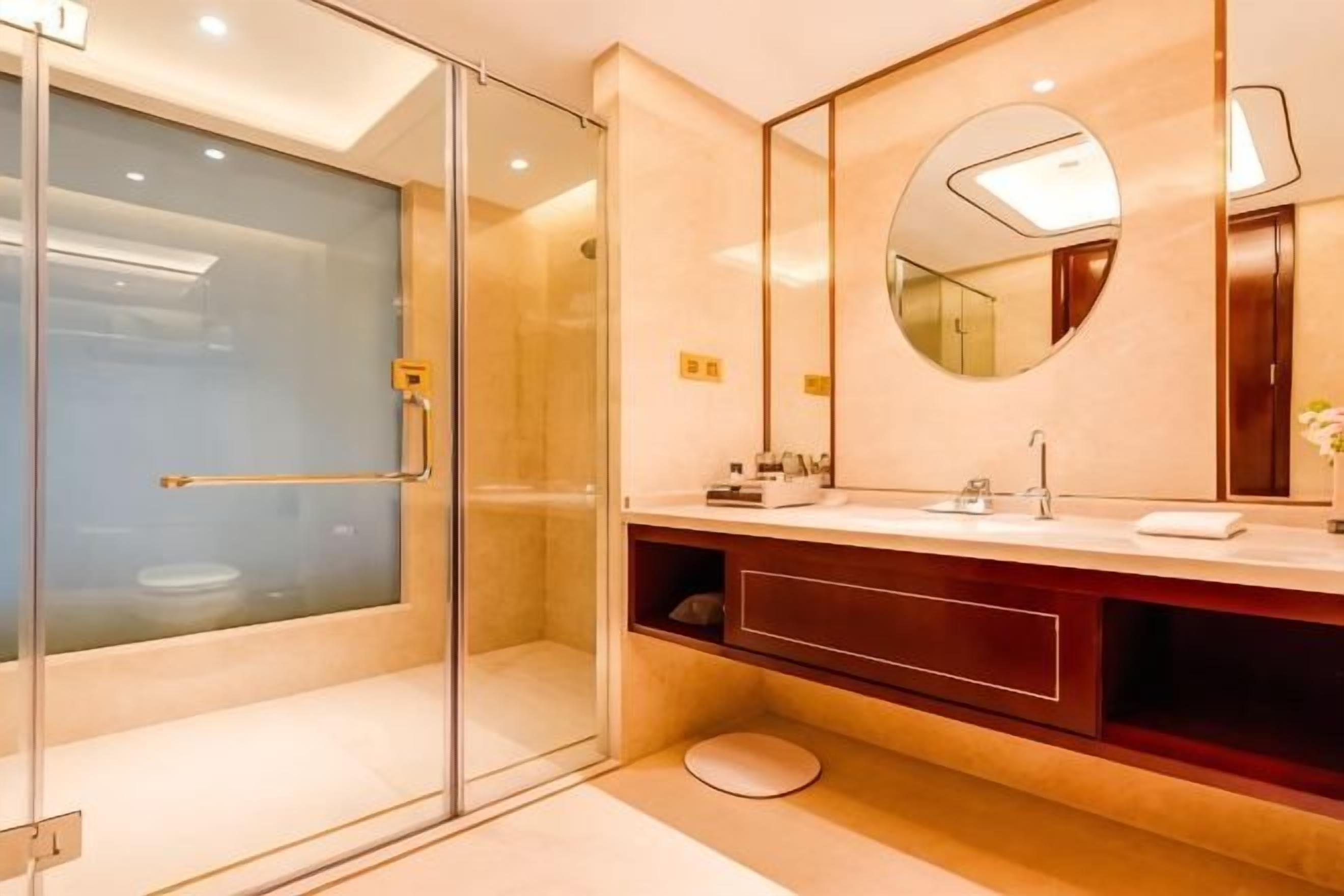 A modern bathroom with a glass-enclosed shower, a round mirror, and a vanity with a sink.
