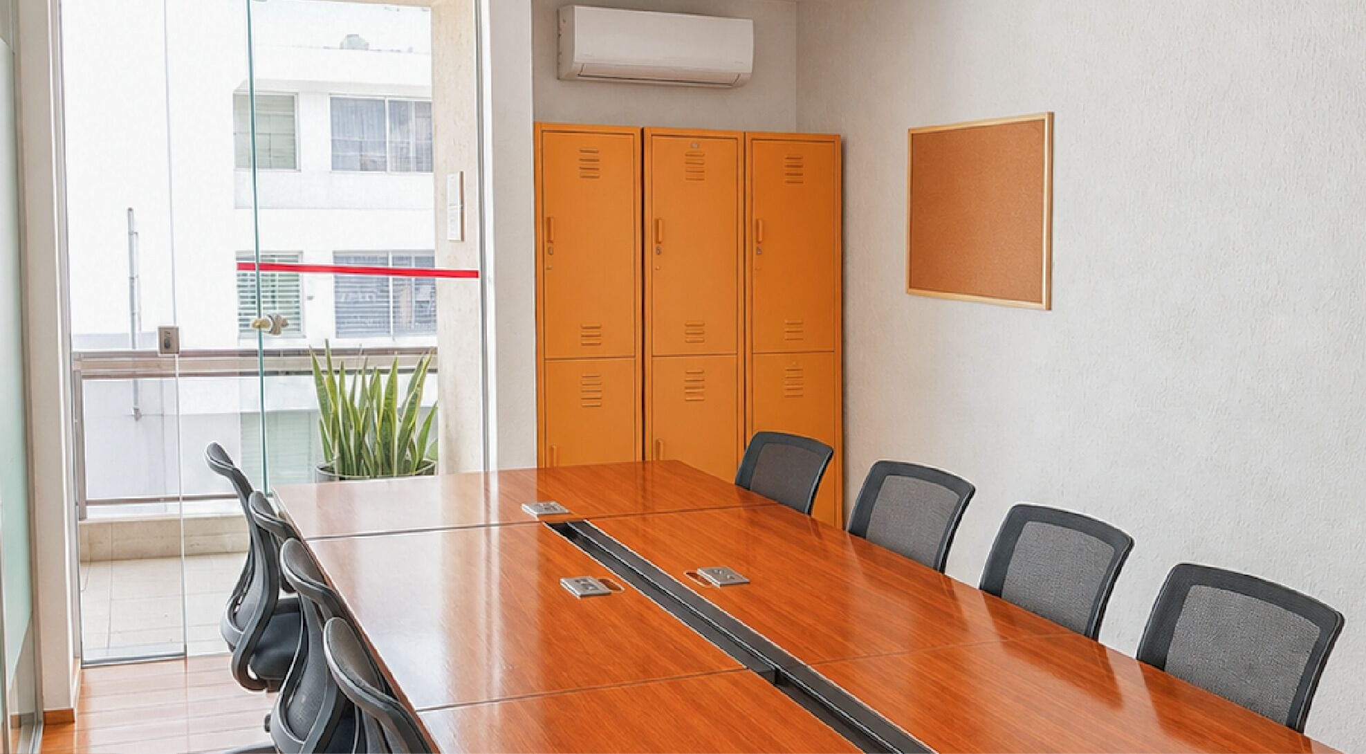 Un salón de conferencias con una mesa de madera, seis sillas y un ventanal con vistas a edificios.