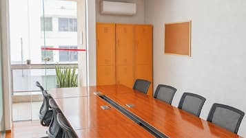 Un salón de conferencias con una mesa de madera, seis sillas y un ventanal con vistas a edificios.