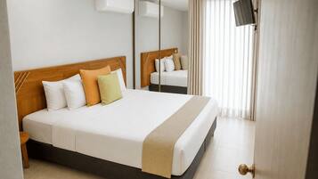 A hotel room with a large bed, a mirror, a television, and a door with a golden handle.