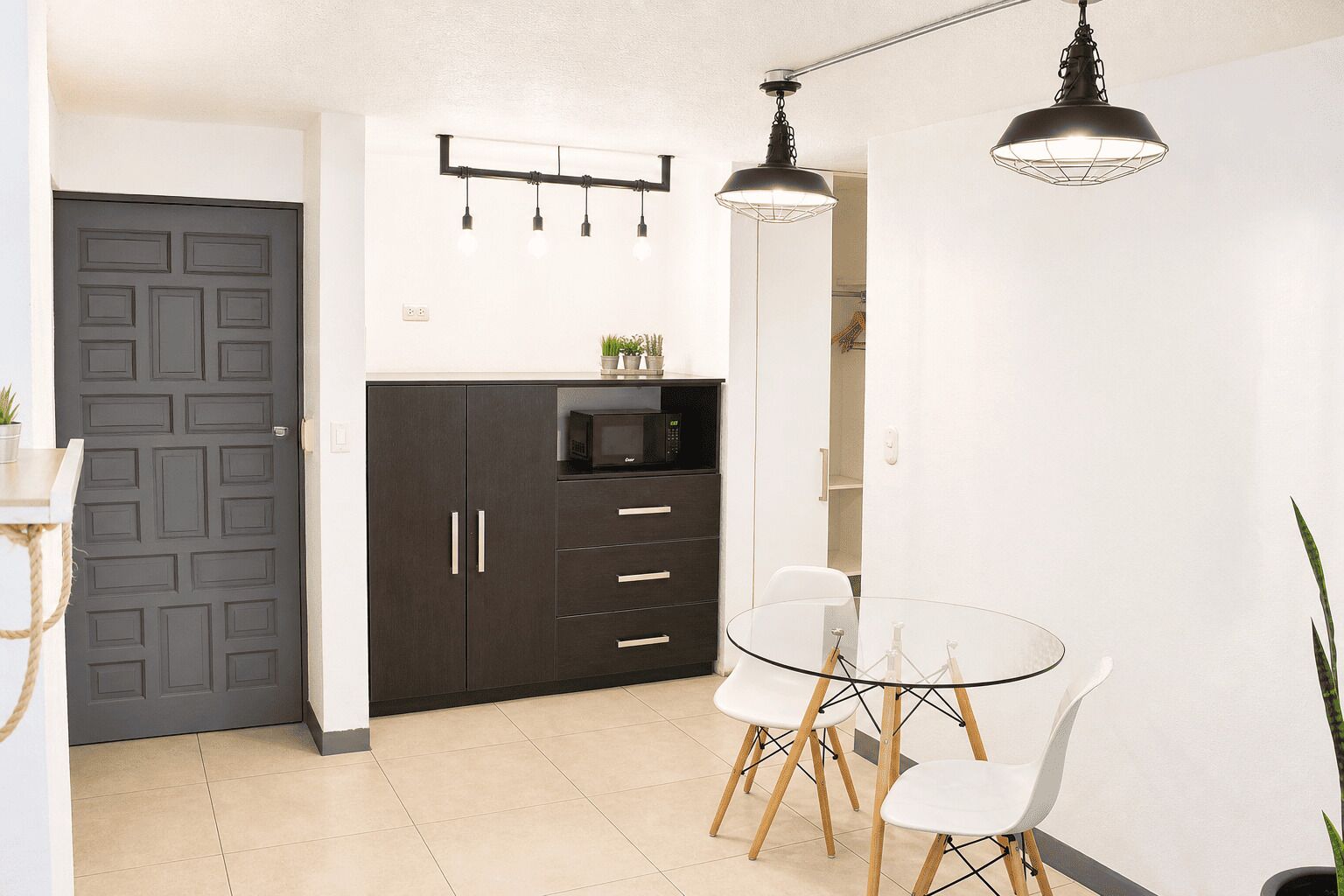 Una cocina moderna con armarios oscuros, microondas y una mesa de comedor de vidrio con sillas.