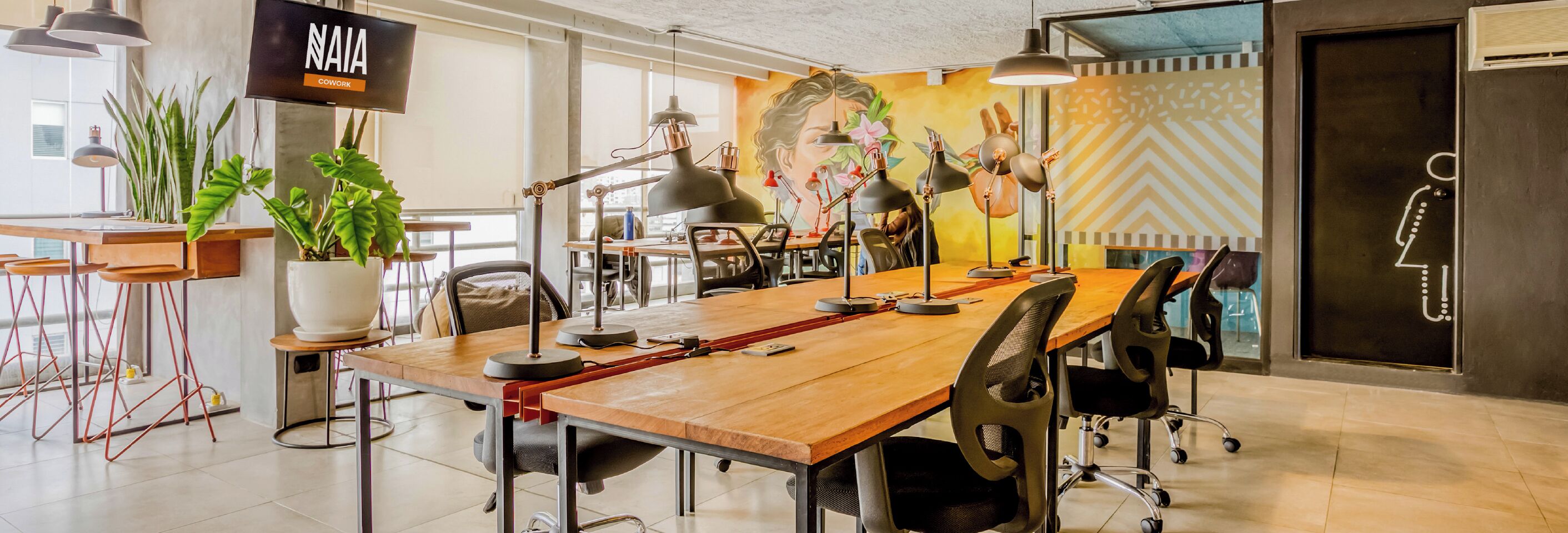 Un espace de travail partagé moderne, doté d’une grande table en bois, de nombreuses chaises et de différents modèles de lampes de bureau.