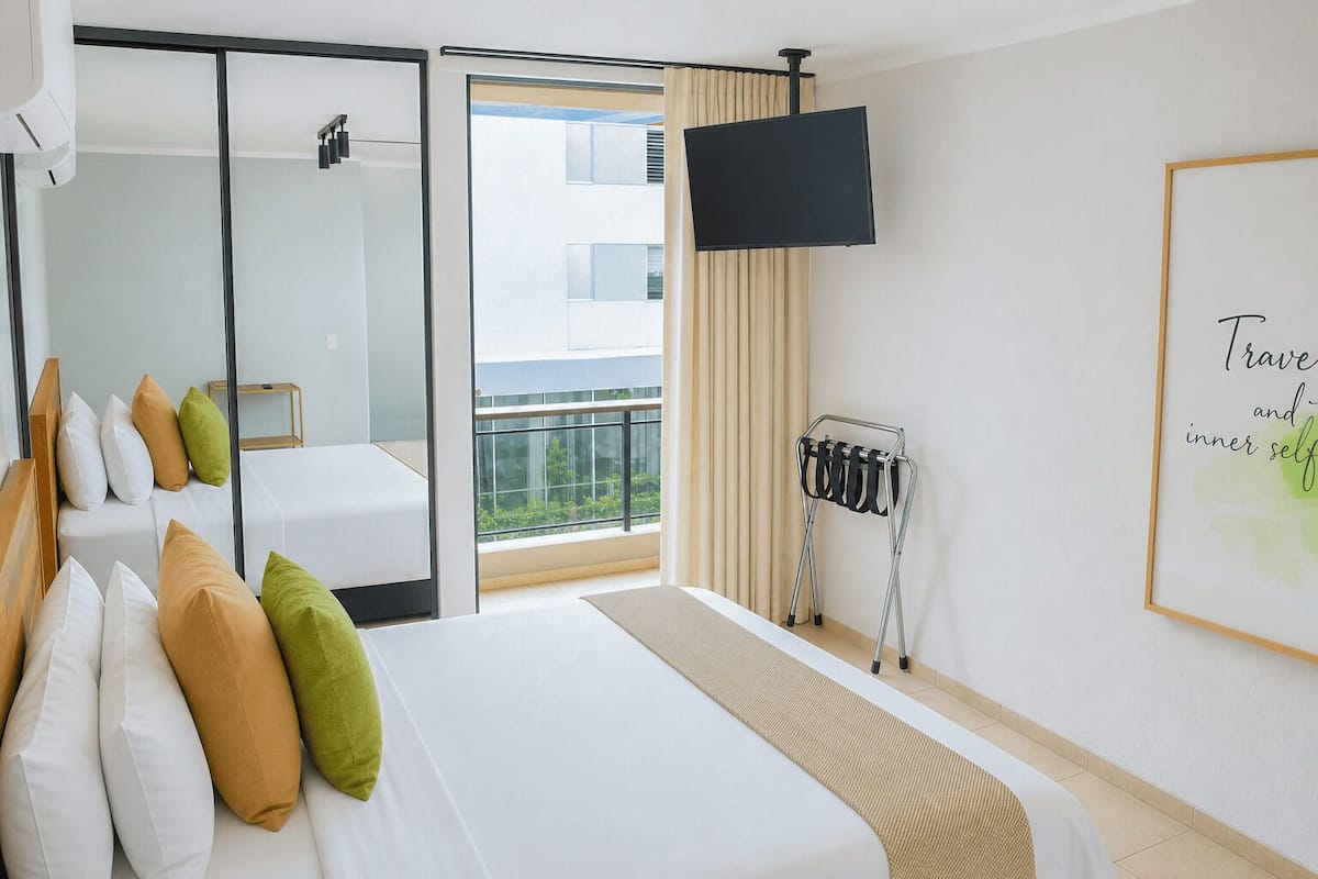 Hotellihuone, jossa on sänky, televisio, peili, ikkuna, josta on näkymä, ja seinä, jossa on kehystetty sitaatti.