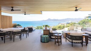Un patio al aire libre con vista al océano, que incluye una mesa redonda, sillas y un sofá.