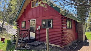 A red log cabin with a front porch, a small window, and a door.