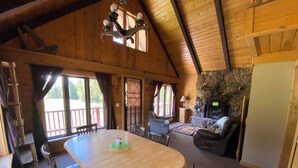 A wooden cabin interior with a dining table, chairs, a fireplace, and a balcony.