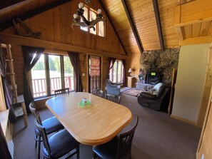 A wooden interior with a dining table, chairs, a fireplace, and a balcony.