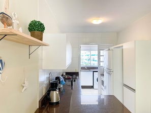 A modern kitchen with white cabinets, a stainless steel kettle, and a built-in oven. - Residencial Porto da Brava (Florianopolis)