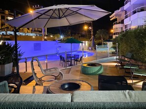An outdoor pool area with lounge chairs and umbrellas, surrounded by a low wall and a building in the background. - Residencial Porto da Brava (Florianopolis)