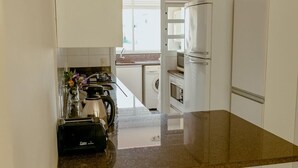 Une cuisine moderne avec des meubles blancs, un plan de travail en granit, une machine à café et un lave-linge à l’arrière-plan.