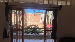 Une porte surmontée d’un portail en métal qui donne sur un espace extérieur agrémenté d’un mur en briques, de plantes en pot et d’un parasol rouge.