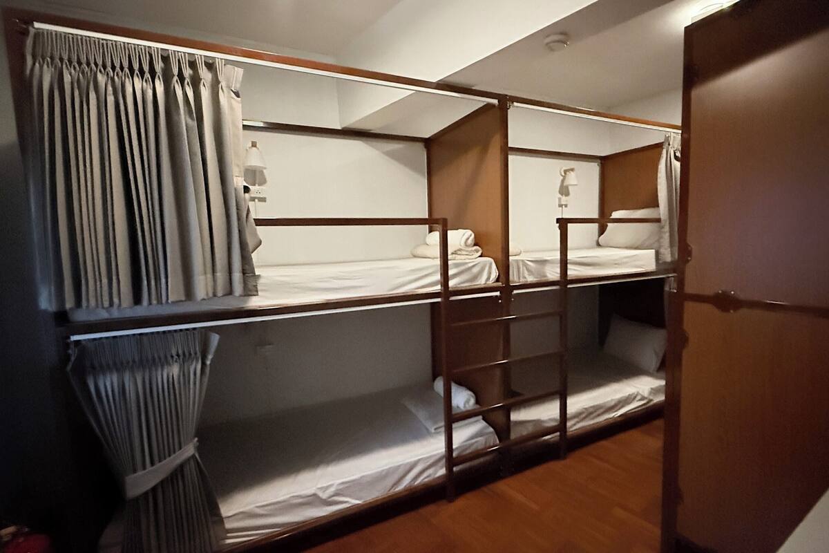 A bunk bed room with curtains, a bedside table, and a wooden door.