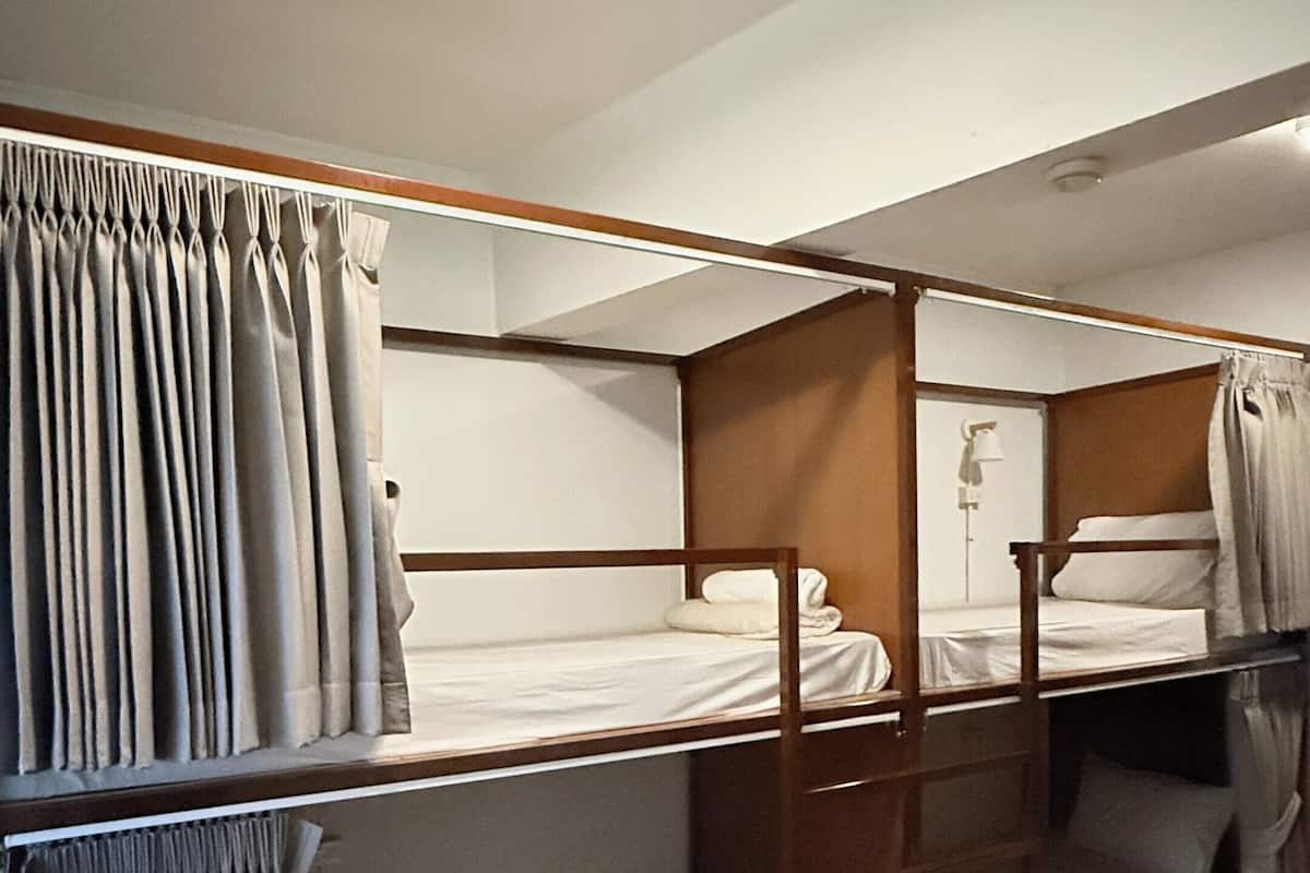 A bunk bed room with curtains, a ceiling light, and wooden flooring.