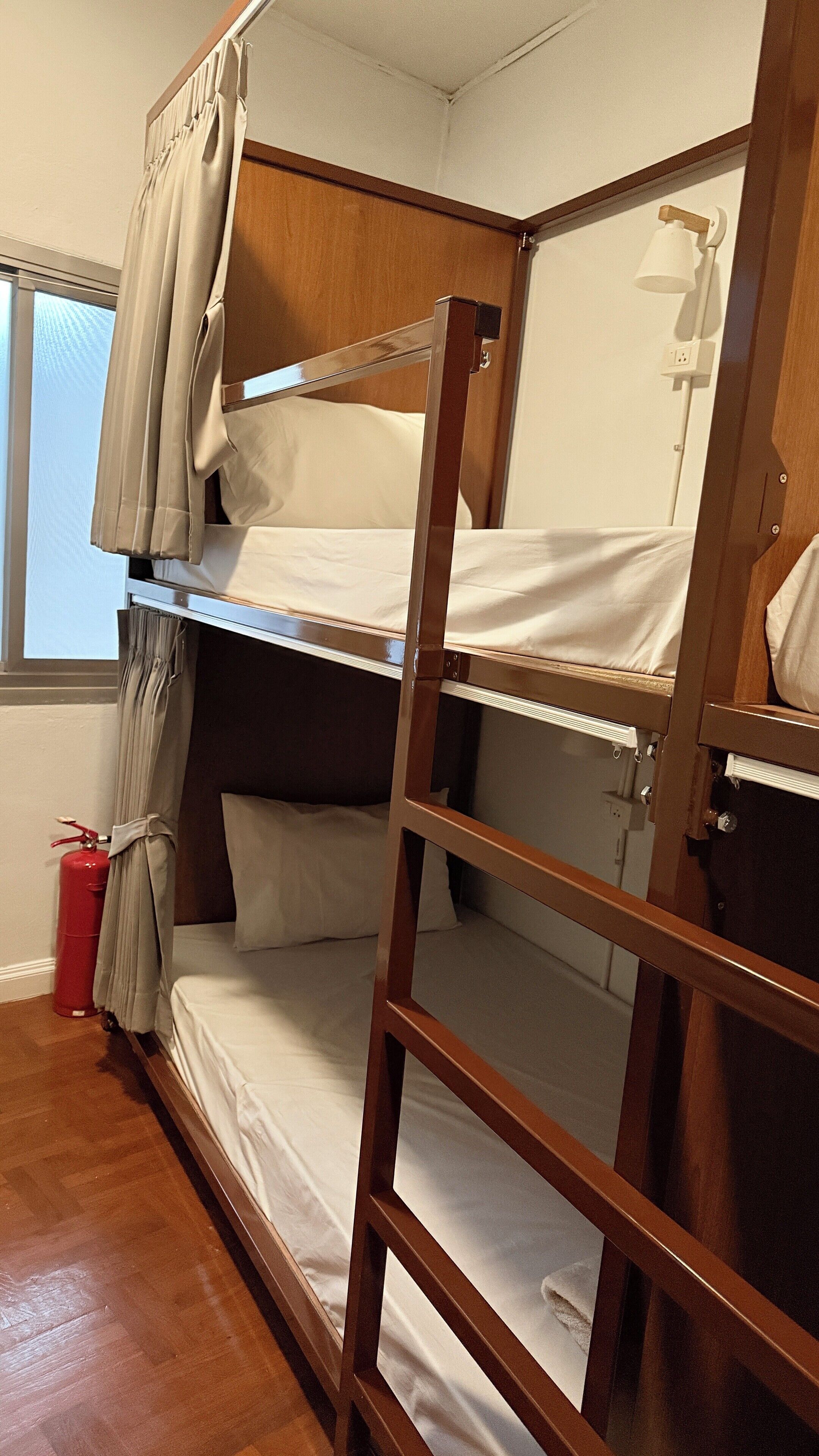 A bunk bed with a wooden frame, white bedding, and a window with curtains.