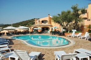 A pool area with lounge chairs, umbrellas, and a building with a tiled roof. - Residence with swimming pool near Budoni (Budoni)