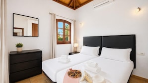 A hotel room with two beds, a dark dresser, a mirror, a window with curtains, and a small plant.