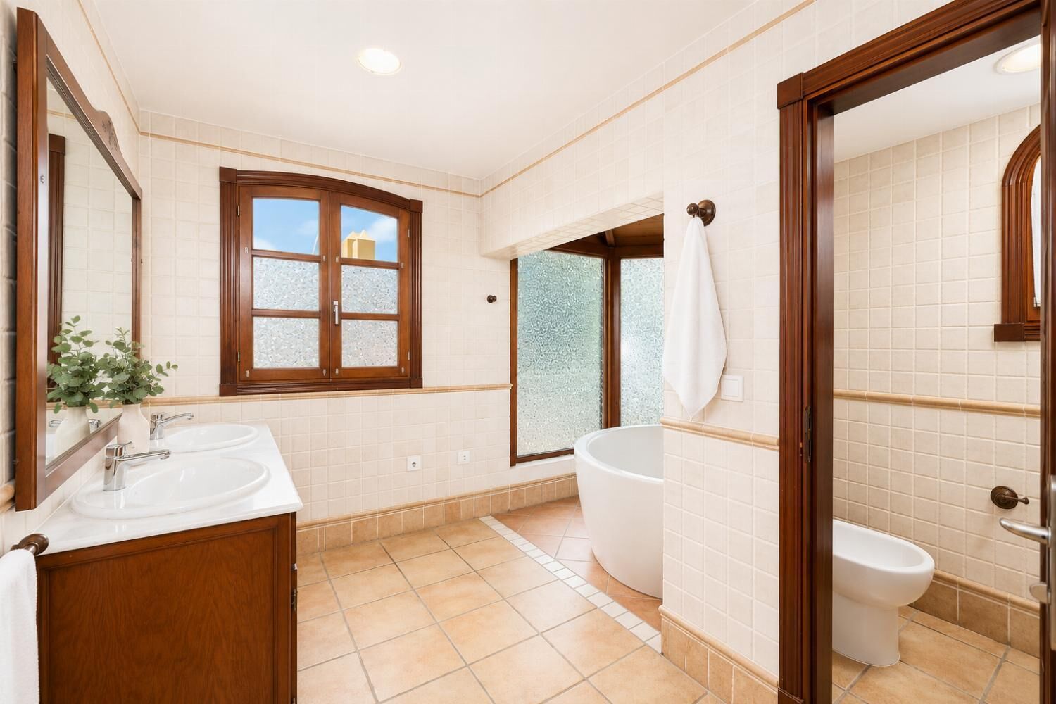 A bathroom with two sinks, a bathtub, a toilet, a window, and a mirror.