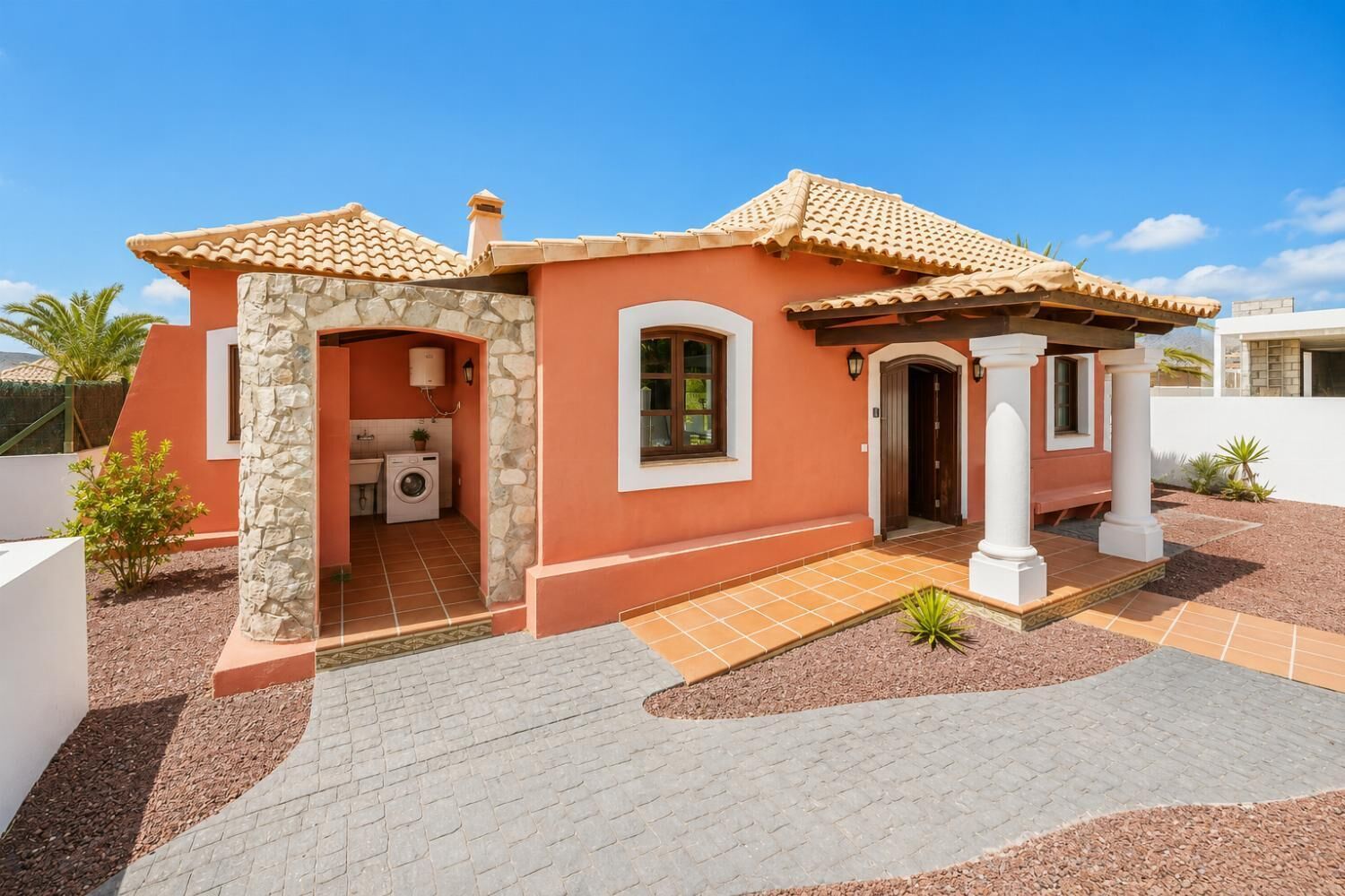 A two-story house with a stone facade, a tiled roof, and a small porch with columns.