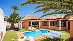 A house with a swimming pool, two lounge chairs, and a ping pong table.