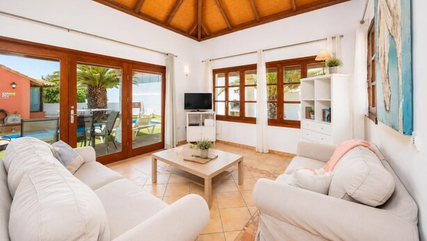 A living room with a TV, white sofas, a coffee table, and a view of the outside.